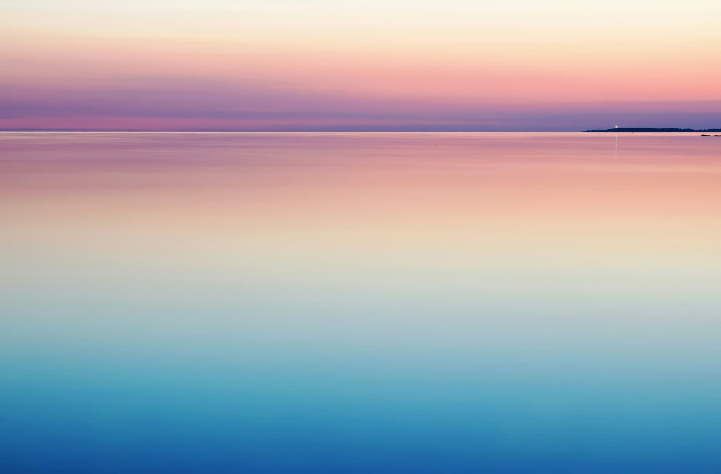 A calm sea at dawn, a lighthouse light on the horizon